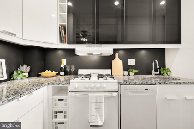 kitchen featuring white appliances, white cabinetry, under cabinet range hood, light stone counters, and a sink