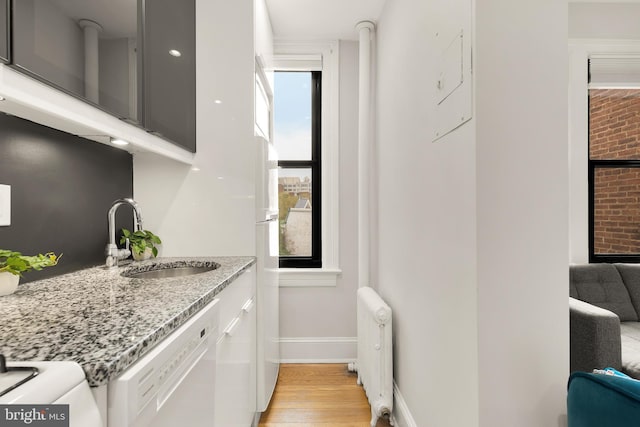 interior space featuring light wood-type flooring, cabinet space, a sink, baseboards, and radiator heating unit