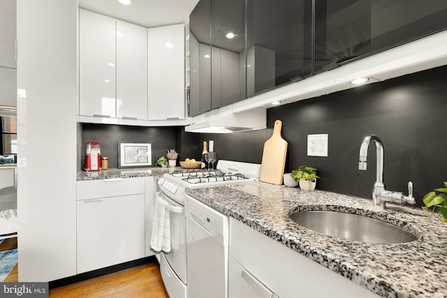 kitchen featuring light stone countertops, gas range, white cabinetry, under cabinet range hood, and a sink