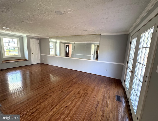 spare room with wood finished floors, visible vents, a healthy amount of sunlight, crown molding, and a textured ceiling