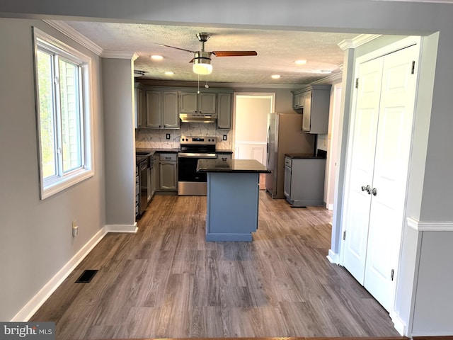 kitchen featuring crown molding, dark countertops, gray cabinets, stainless steel appliances, and under cabinet range hood
