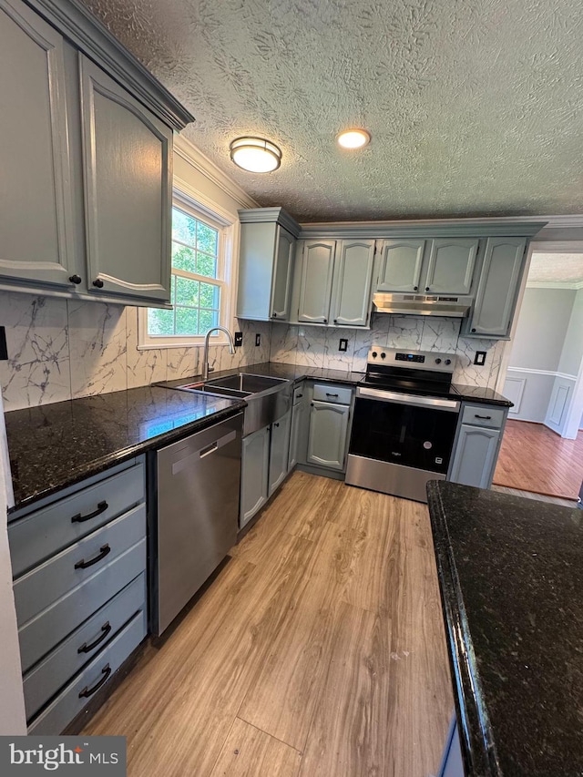 kitchen featuring a sink, a textured ceiling, appliances with stainless steel finishes, light wood-style flooring, and under cabinet range hood