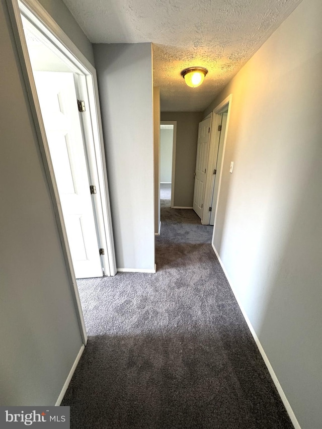 hall with baseboards, carpet, and a textured ceiling