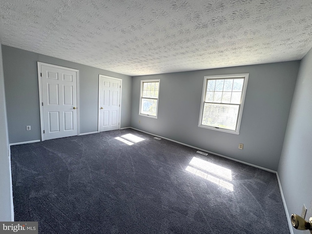 unfurnished bedroom featuring dark carpet, baseboards, visible vents, and a textured ceiling
