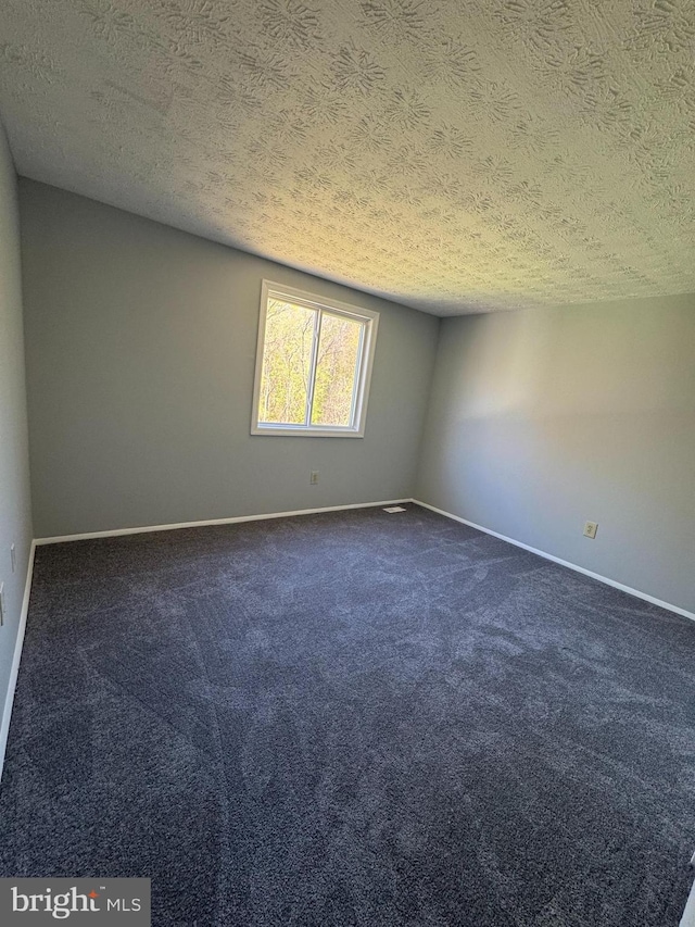 spare room featuring dark carpet, baseboards, and a textured ceiling