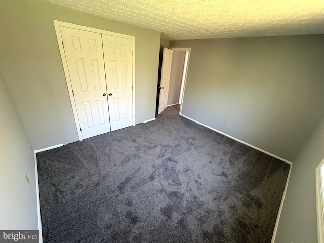 unfurnished bedroom with dark colored carpet, baseboards, a textured ceiling, and a closet