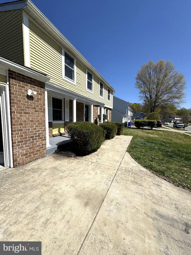 view of property exterior with brick siding, a porch, and a yard