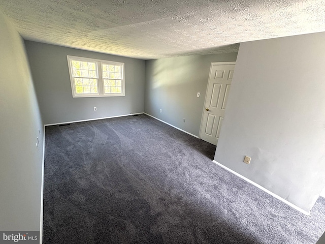 unfurnished room with dark carpet, baseboards, and a textured ceiling