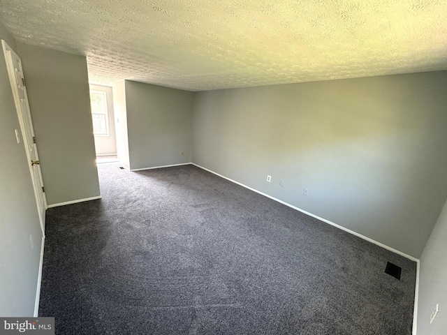 spare room with dark carpet, baseboards, a textured ceiling, and visible vents