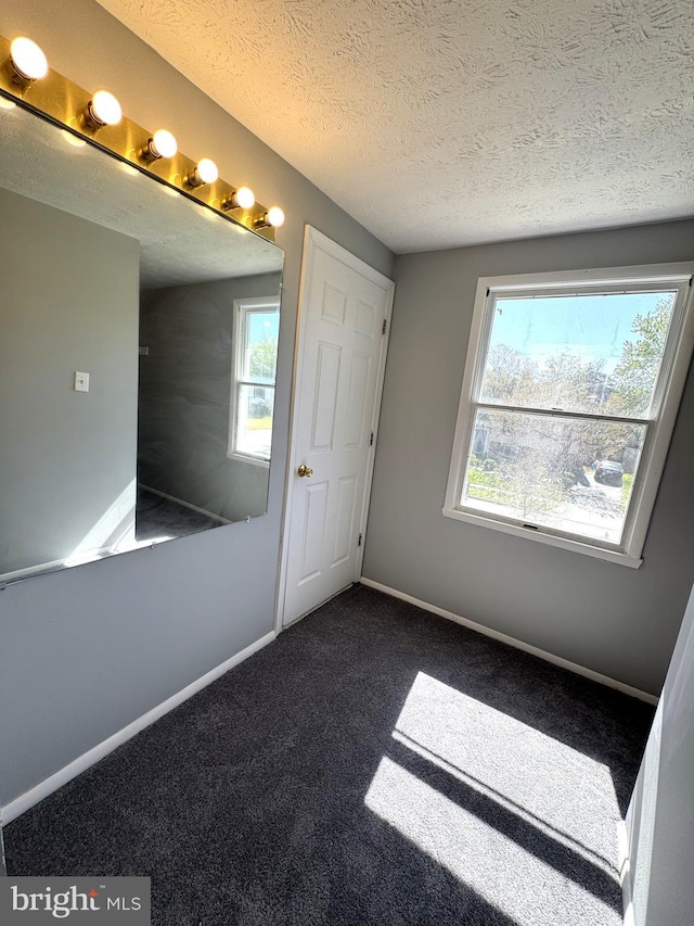 unfurnished bedroom featuring dark colored carpet, baseboards, a textured ceiling, and multiple windows