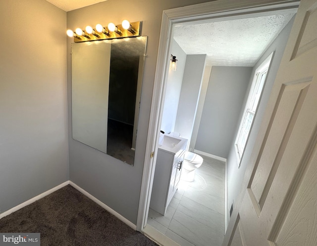 bathroom featuring baseboards, a textured ceiling, toilet, and vanity