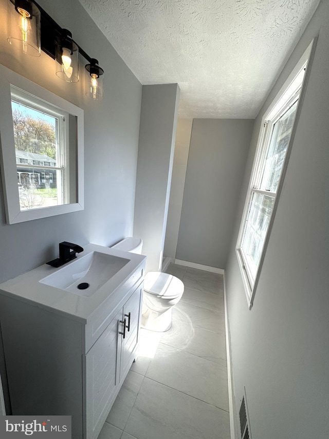 half bathroom with toilet, vanity, a textured ceiling, and visible vents