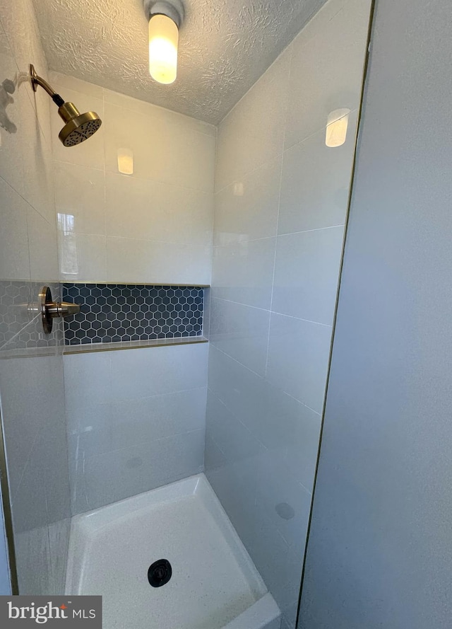full bath featuring a textured ceiling and tiled shower