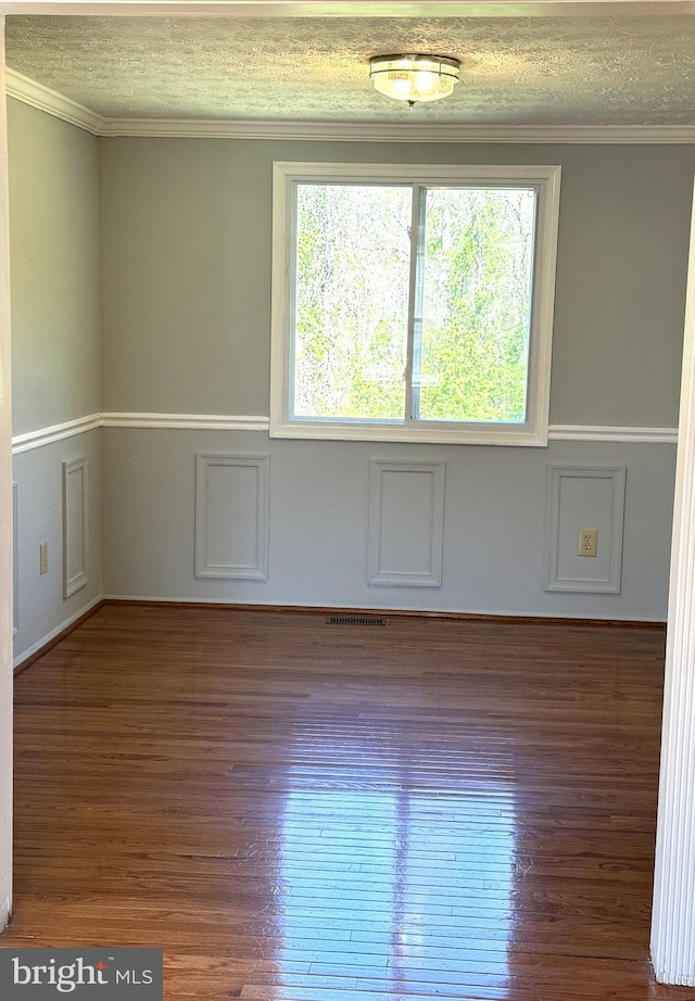 empty room with wood finished floors, visible vents, a textured ceiling, and ornamental molding