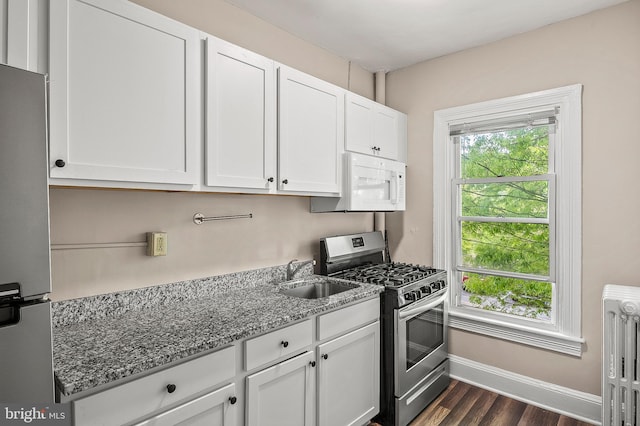 kitchen featuring appliances with stainless steel finishes, radiator, stone counters, a sink, and baseboards