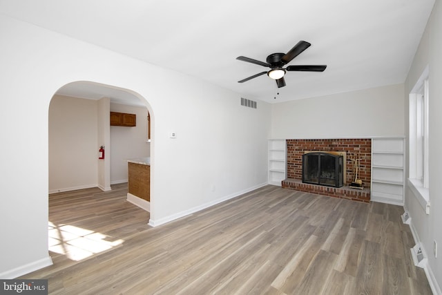 unfurnished living room with visible vents, arched walkways, light wood-style floors, and ceiling fan