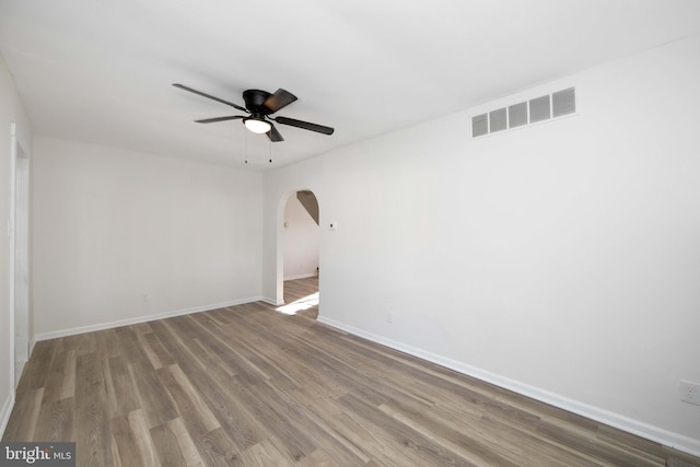 unfurnished room with a ceiling fan, arched walkways, wood finished floors, and visible vents