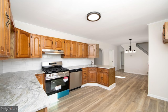kitchen with a sink, a chandelier, appliances with stainless steel finishes, a peninsula, and under cabinet range hood