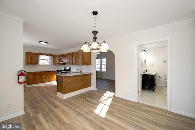 kitchen with a notable chandelier, brown cabinetry, light wood-style flooring, under cabinet range hood, and arched walkways