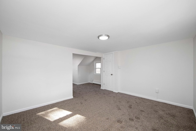 empty room with a baseboard radiator, vaulted ceiling, baseboards, and carpet