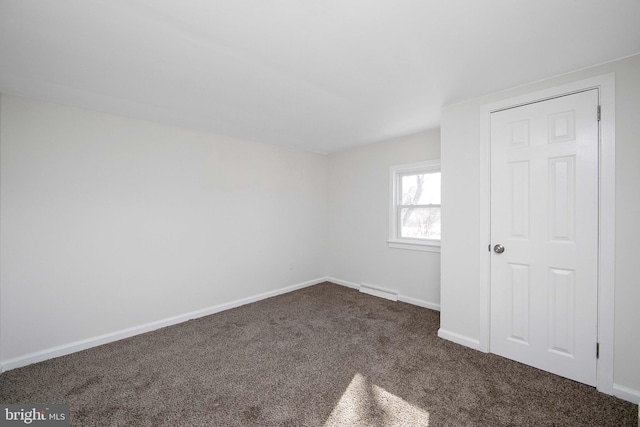 unfurnished bedroom featuring baseboards, dark colored carpet, and visible vents