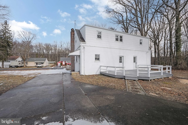 rear view of property with concrete driveway, stucco siding, a deck, and a chimney