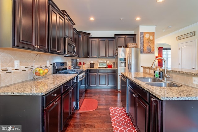 kitchen featuring stainless steel appliances, arched walkways, a sink, dark wood finished floors, and decorative backsplash