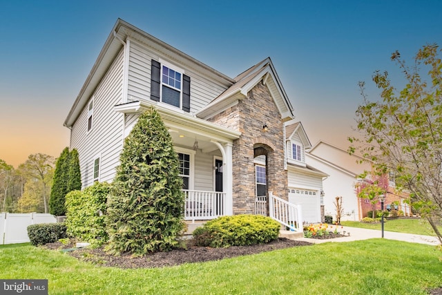 traditional-style home featuring a lawn, a porch, stone siding, and fence