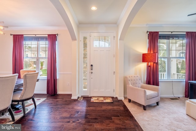 foyer featuring arched walkways, ornamental molding, wood finished floors, and baseboards