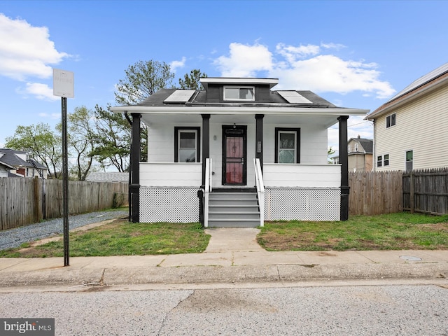 bungalow with roof mounted solar panels, a porch, and fence private yard