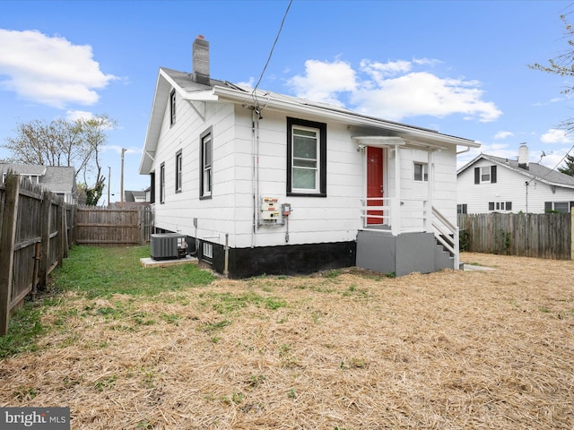 back of property with a fenced backyard, a lawn, a chimney, and central AC