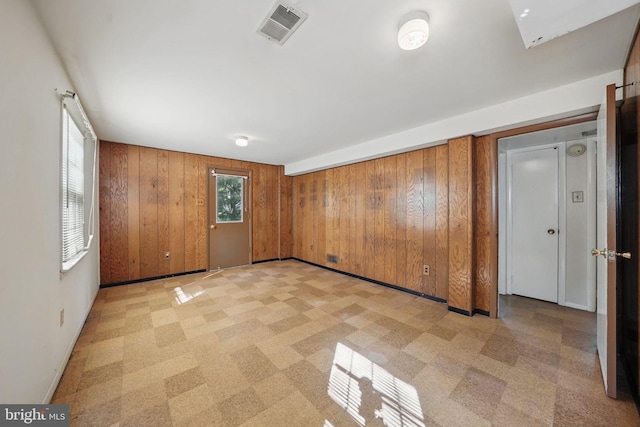 empty room with wooden walls, light floors, baseboards, and visible vents