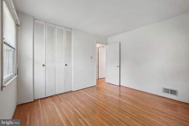unfurnished bedroom with light wood-style floors, a closet, and visible vents