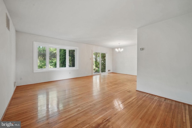 empty room with light wood-type flooring, a notable chandelier, and visible vents