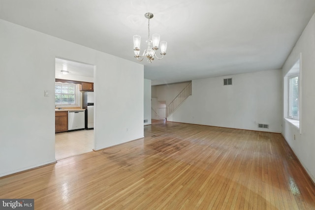 unfurnished living room with light wood-style floors, stairway, a notable chandelier, and visible vents