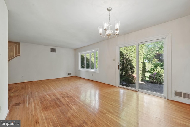 spare room with a chandelier, light wood-style flooring, and visible vents