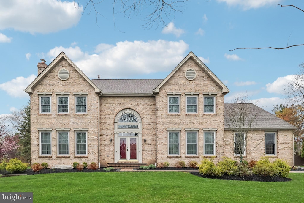 traditional-style home with a shingled roof, brick siding, a chimney, and a front lawn