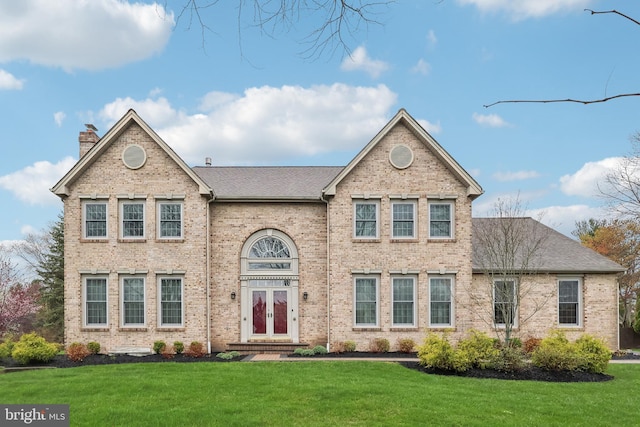 traditional-style home with a shingled roof, brick siding, a chimney, and a front lawn