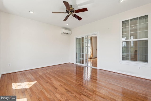 empty room with a wall mounted air conditioner, ceiling fan, baseboards, and wood finished floors