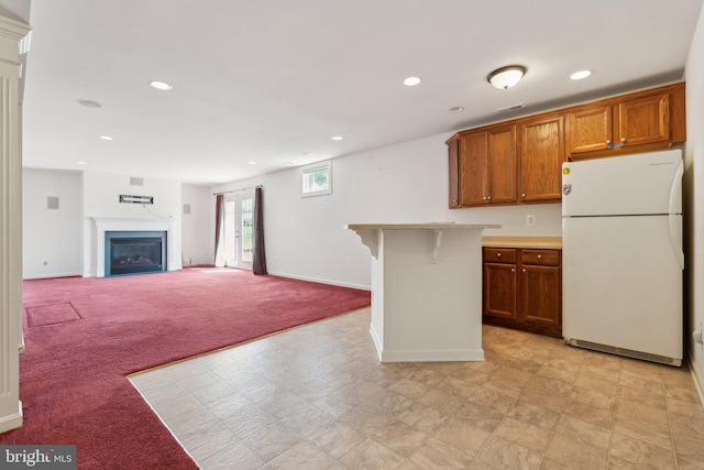 kitchen with brown cabinetry, freestanding refrigerator, a fireplace, a kitchen bar, and recessed lighting