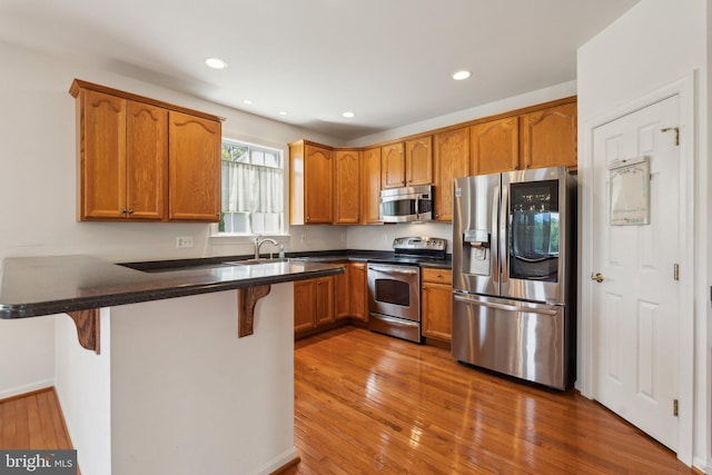 kitchen featuring a peninsula, a breakfast bar area, wood finished floors, brown cabinetry, and appliances with stainless steel finishes