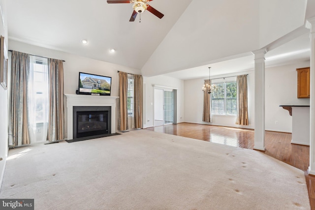 unfurnished living room featuring a fireplace with flush hearth, ornate columns, visible vents, high vaulted ceiling, and ceiling fan with notable chandelier