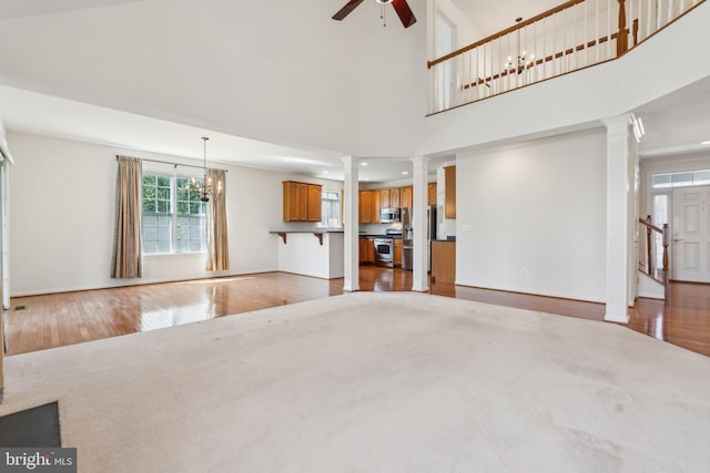 unfurnished living room featuring ceiling fan with notable chandelier, baseboards, light wood-type flooring, and decorative columns