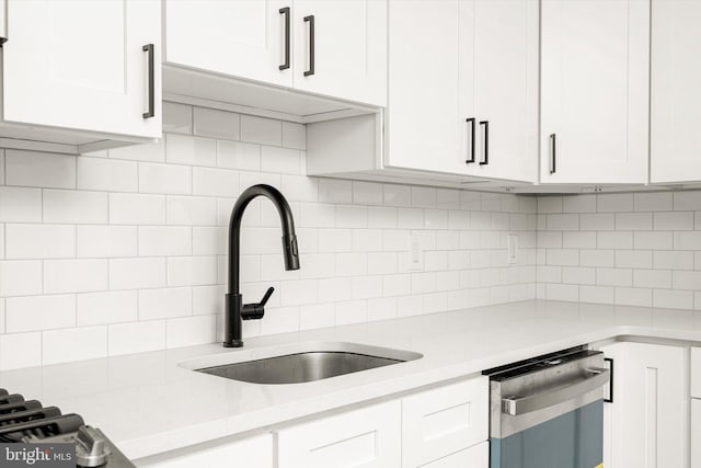 kitchen with tasteful backsplash, light stone countertops, dishwasher, a sink, and white cabinetry