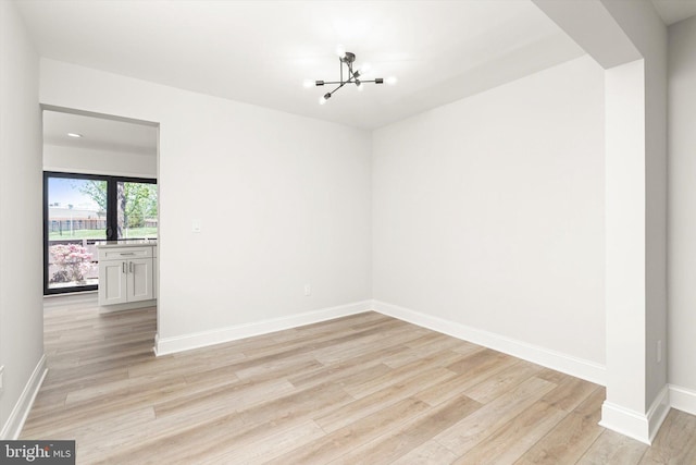 spare room featuring baseboards, an inviting chandelier, and light wood finished floors