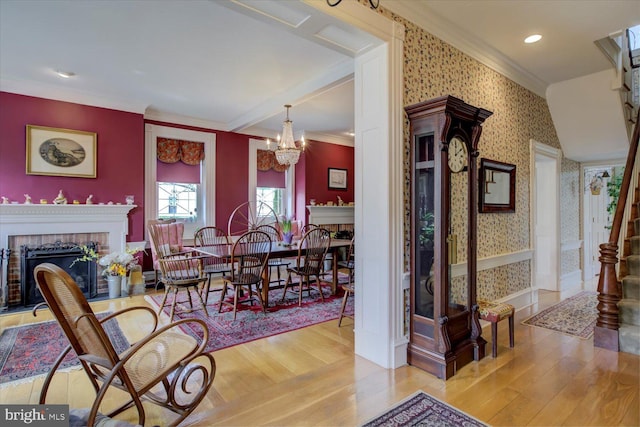 dining area with a chandelier, a fireplace, crown molding, wallpapered walls, and wood finished floors