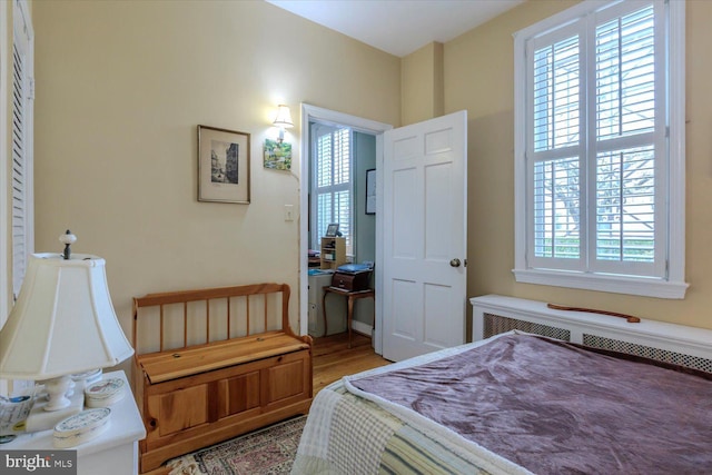 bedroom with radiator, wood finished floors, and multiple windows