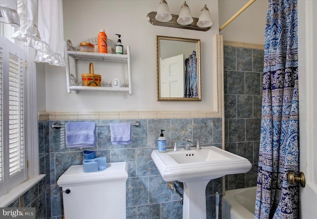 bathroom featuring toilet, tile walls, shower / bath combo, and wainscoting