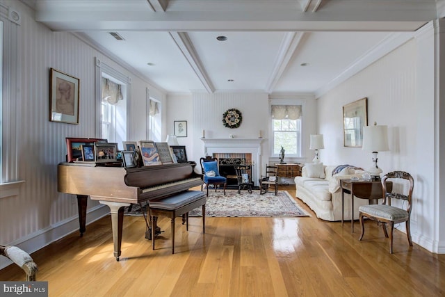 living area with visible vents, beamed ceiling, light wood-style floors, and a brick fireplace