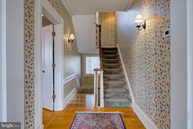 staircase with wood finished floors and wallpapered walls